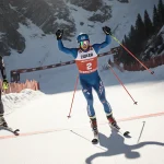 Jan Zabystran crossing the finish line in first place with arms raised on a snowy Val Gardena slope during the World Cup supe