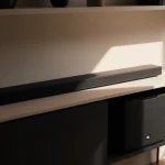 Soundbar positioned on minimalist console with warm lighting highlighting sleek lines and subtle subwoofer shadow