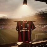 Vintage Nottingham Forest jersey hanging on a wooden dowel with a lone spotlight in a dim stadium honoring John Robertson