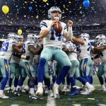 Justin Herbert holding the football with left hand bandaged while teammates lift him amid confetti and crowds at SoFi Stadium