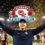 Alabama coach Kalen DeBoer raising his arms in victory with confetti exploding and the Rose Bowl logo shining behind him