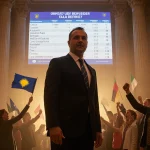Prime Minister Kurti stands confidently with election results screen and cheering supporters waving flags in golden-lit Kosov