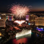Fireworks explode above the Fontainebleau hotel with neon lights and Bellagio fountains reflecting sunset glow