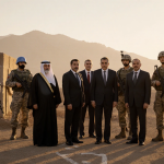 Diplomats standing together with soldiers and peacekeepers near a decommissioned bunker and mountains behind