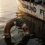 Life ring floats upright in murky Lake Superior waters with rusted metal and barnacles near the decrepit hull of the Edmund F