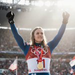 Lindsey Vonn standing on Olympic podium with gold medal gleaming around her neck and titanium knee under suit among fans.