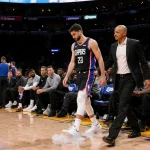 Luka Doncic injured walking toward locker room with left leg wrapped in ice and trainers beside him Clippers players watch.