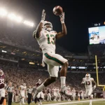 Malachi Toney leaps to catch a touchdown pass with Miami Hurricanes logo under stadium lights scoreboard reads 10-3.