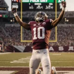 Malachi Toney celebrating touchdown catch with quarterback kneeling and scoreboard glow in sunset background