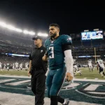 Marcus Mariota walking away from field with ice wrapped hand and trainer support under bright stadium lights