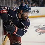 Mason Marchment crashes into the boards with Blue Jackets logo and Seattle Kraken branding and warm glow