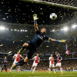 Matvei Safonov diving to the right for a penalty save with confetti and stadium lights swirling behind.