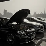 Mercedes-Benz parked with hood open showing tangled wires and machinery at an emissions testing station with industrial haze.