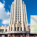 Art Deco skyscraper gleams above downtown Miami with American flags and Trump banners and city map pin marking transfer site.