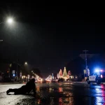 Streetlight illuminates a vehicle silhouette with Austin Police patrol car and Christmas lights reflected on wet pavement