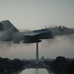 Military aircraft soaring through foggy dusk sky with National Mall silhouette and Washington Monument in distance.