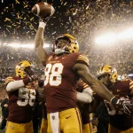 Smith holding the football for victory with teammates rushing to congratulate him under bright stadium lights and confetti