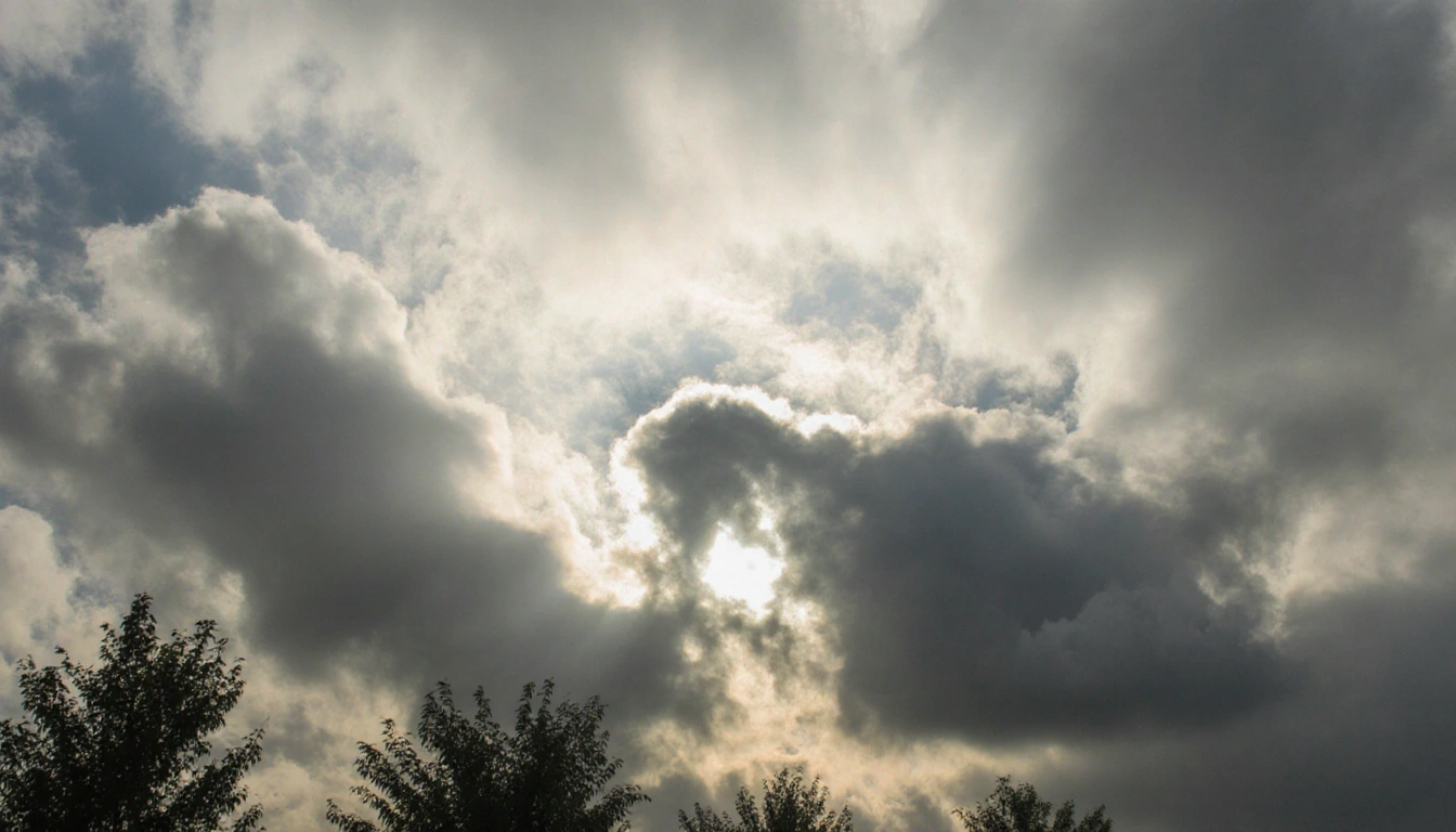 Leaves rustle in scattered trees against a partly sunny cloudy sky with sunbeams peeking through thick white clouds