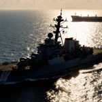 Destroyer cutting waves with propellers and a Coast Guard cutter beside it waving a red and white flag, a distant cargo ship