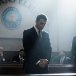Nick Reiner standing at courthouse looking down with lawyer beside him and spotlight on his face in a courtroom scene