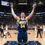 Nikola Jokic celebrating after scoring 56 points and holding up his jersey with confetti and fans cheering in the background.
