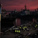 Emergency responders crouch near scattered missiles with the Ukrainian flag fluttering over the quiet port.