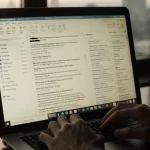 Old laptop showing mixed news and personal emails with soft warm lighting and a distant cityscape.