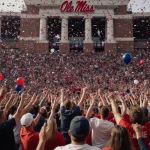Fans cheering wildly with confetti and balloons in Vaught-Hemingway Stadium Ole Miss columns and brick façade showing victory