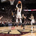 Oscar Cluff dribbling basketball mid‑air with three‑pointer and Braden Smith celebrating as confetti rains over Purdue bench