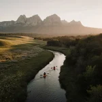 Kayakers paddling through a calm creek with wildflower hills and misty Palo Pinto Mountains in the background
