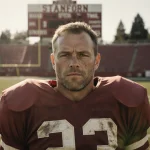 Paul Wiggin standing heroically on Stanford football field with scoreboard and sunlit face