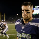Philip Rivers watches the field with a disappointed expression as a Seattle tackle occurs in the background.