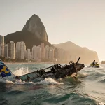 Submerged ultralight plane wreckage drifts with floating debris near Christ the Redeemer under golden sunset.