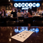 Winners cheering with the glowing TV jackpot and a lone Powerball ticket showing numbers 58 28 31 1 57