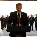 President Trump standing at podium with grieving families near Dover Air Force Base hangar during winter mourning ceremony