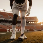 Quintrevion Wisner stands on University of Texas football field at dusk with a worn cleat in focus and golden light highlight
