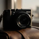 Camera resting on vintage leather travel bag with warm natural light and subtle cityscape background.