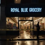 Police officer guarding open doors of Royal Blue Grocery with Texas Capitol at dusk