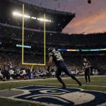 Jason Myers kicks a field goal with illuminated Seattle Seahawks logo and the 18-16 scoreboard on football field at sunset