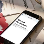 Smartphone screen shows blocked app message with Texas flag overlay and coffee on cluttered desk