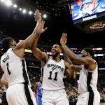 Spurs players high-fiving with Wembanyama center while scoreboard reads 117-102 Thunder bench looks festive lights