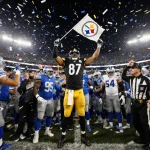 Steelers defensive back raising arms in triumph with referee holding flag and Lions sideline chaos.