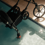 Stroller resting near pool with upside-down walker and a leg poking out of water.