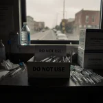 Two syringe boxes display a DO NOT USE label on one and fresh supplies on the other in a dim storage room