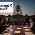 Voters discuss ballots with pens on a table and a screen showing Amendment X under light above the Texas State Capitol