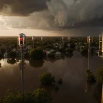Warning sirens illuminating flooded Texas landscape with green floodplain and evacuating residents