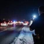 State trooper holding radar gun under spotlight with patrol cars parked on Texas winter highway