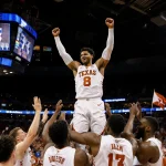 Texas Longhorns player hoisted above teammates with arms raised in victory while fans wave flags in packed arena
