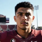 Thomas Castellanos stands on Florida State campus with sun‑kissed background of Doak Campbell Stadium and determined gaze