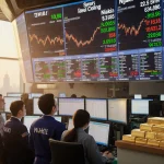 Traders looking at computer screens with Nikkei ticker and precious metal prices glow.